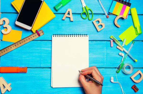 the student writes pen in a notebook. top view. flat lay. school supplies in the school desk, stationery, education concept, blue background, creative chaos, space for text, markers, pens, notepads, stickers.