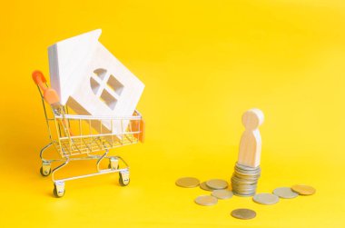 tahtadan adamın sikkeleri bir ev ve bir süpermarket sepetten arka plan üzerinde durmak. Emlak kavramı. Satın alma, satış ve bir ev kiralama. Kredi bir daireye, ipotek oranı için. Genç aileler için uygun fiyatlı konut.