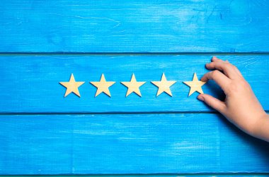 The hand puts the fifth star. The critic determines the rating of the restaurant, hotel, institution. Quality mark. Overview. Five wooden stars on a blue background. A new level of the rating clipart