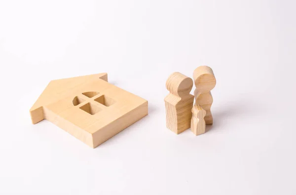 Figures of people stand near a fallen wooden house on a white background. The concept of a natural disaster, the loss of housing. The family was left without a home. The property. Unit of society.