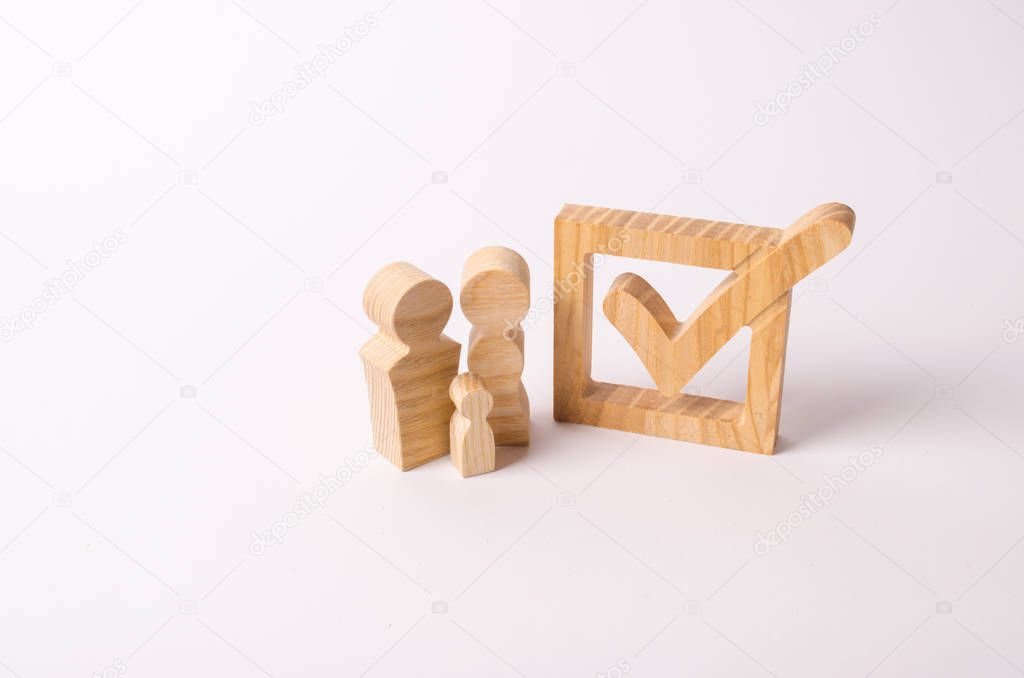 Wooden figures of people stand near the tick in the box. Checkbox. People vote in elections, a referendum. Democratic process, participation in government elections. Setting goals.