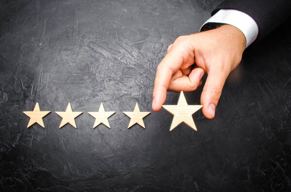 Рука бизнесмена в костюме держит пятую звезду. Получи пятую звезду. Концепция рейтинга гостиниц и ресторанов, оценка критиков и посетителей. Уровень качества, селективная направленность
