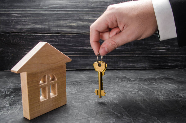 The realtor's hand holds the keys to the house. Wooden house. The concept of buying and selling the apartments, pokin and renovation of the house. Private property, purchase agreement.