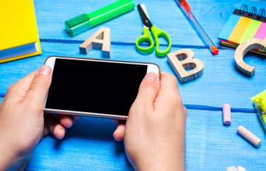 Öğrenci yaratıcı dağınık masaüstü arka planda bir cep telefonu tutuyor. Öğrenci çalışma alanı. Öğrenci ödev yapmak tembel. Eğitim uygulama telefon bağımlılığı