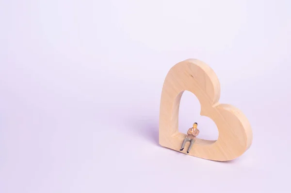 A man sits on a wooden heart and waits. A lonely person is looking for a soul mate, a partner. Site for dating. The concept of love, separation, loneliness