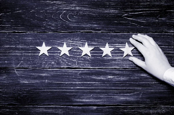 A woman\'s hand puts the fifth star. Quality status is five stars. A new star, achievement, universal recognition. Wooden stars on a black background.