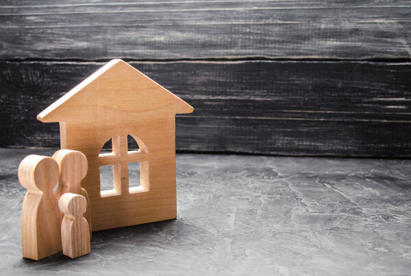 A young family with a child is standing near the house. Wooden house and figures of people. The concept of housing search, rent, purchase. Moving. Loan for housing. A happy family, a dream.