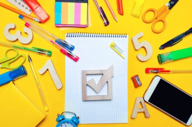 okul seçimleri kavramı. Seçim onay kutusu ve bir masa üzerinde sarı bir arka plan üzerine okul aksesuarları. Eğitim. ileti örneği, saatler, renkli kalemler, telefon, işaretleri. Not defteri. yukarıdan görüntüleyin. kopya alanı. üstten görünüm. düz lay