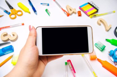 Öğrenci bir cep telefonu beyaz arka planda tutuyor. eğitim kavramı. okula dönüş. yaratıcı karışıklık üstünde okul sırası. Resepsiyon. ileti örneği. Smartphone. metin için yer. düz lay.