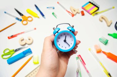 okula dönüş. bir öğrencinin elinde okul masasında mavi çalar saat. ileti örneği. aksesuarlar. Beyaz arka plan. çıkartmalar, renkli kalem, kurşun kalem, makas. yukarıdan görüntüleyin. düz lay.