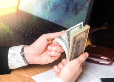 Takım elbiseli bir işadamı bir dizüstü bilgisayar ve mali çizelgeleri elinde bir masada dolar sayar. Bir başarılı bir iş, başarılı satış, tasarruf, yatırım kavramı. Borsası'nda oynarken