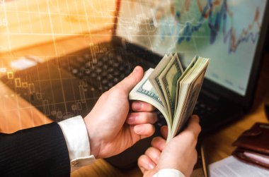 Takım elbiseli bir işadamı bir dizüstü bilgisayar ve mali çizelgeleri elinde bir masada dolar sayar. Bir başarılı bir iş, başarılı satış, tasarruf, yatırım kavramı. Borsası'nda oynarken.