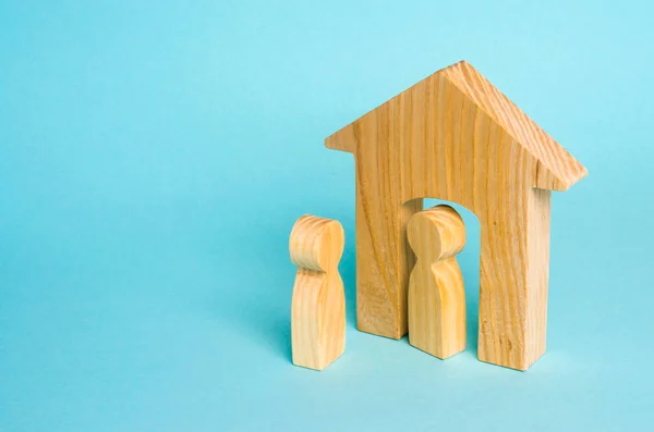 A wooden figure of a man meets a guest on a blue background. Wooden house. The concept of an apartment house, real estate. Buying and selling apartments, affordable housing for families. Protection
