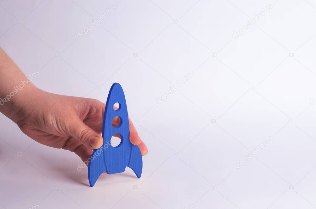 Wooden blue rocket in hand on a white background. A man is playing with a rocket. Minimalism, space travel and tourism, commercial rocket launches into space. The conquest of other planets