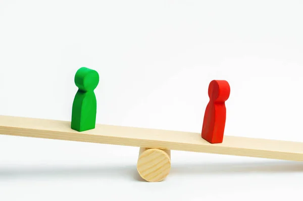 wooden figures of people. rivals in business stand on the scales. trial. conflict. victory and defeat. bad and good worker. the red figure outweighs the green one. concept of success and power. competition