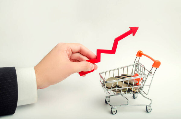 the concept of attracting investments, increasing the average check in the store. The businessman's hand holds the arrow up above the supermarket trolley. growth of the economy. capital building