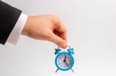 Bir işadamı el Beyaz bir arka plan üzerinde mavi bir çalar saat tutar. Zaman, zaman eylem akışını kavramı. İş saatlik ödemesi. Konaklama için yarı zamanlı çalışma ve iş için geç. Zaman para demektir.