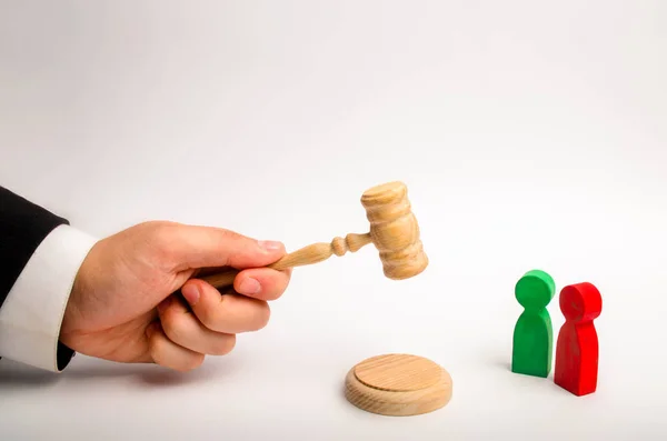 The referee\'s hand holds a hammer and issues a verdict in the dispute between the red and green opponents. court cases, the resolution of disputes and charges between the defendant and the plaintiff.