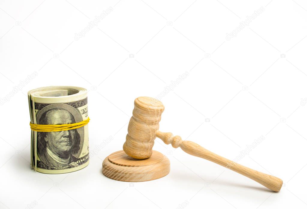 A wooden judge hammer and a bundled bundle of dollars on a white background. Franklin's eyes on the banknote are covered with an elastic band. The concept of corruption in the judicial sphere.