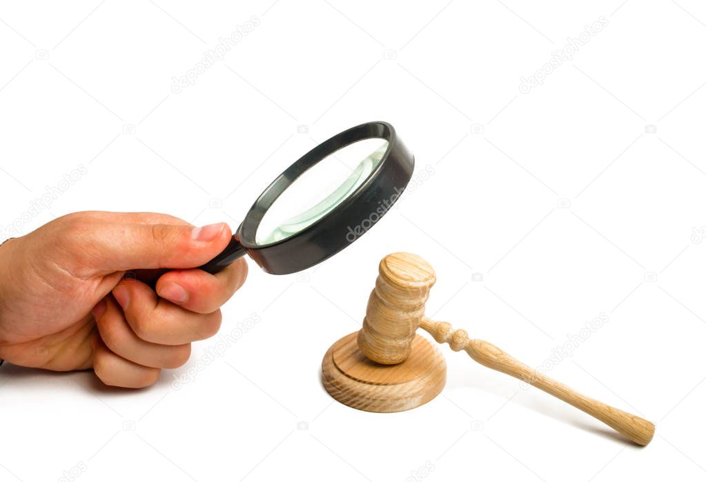 The hand with the magnifying glass gazes intently at the hammer of the judge. The concept of investigation of court cases. Corruption in the courts. Arbitrage practice. Appeal for sentencing.