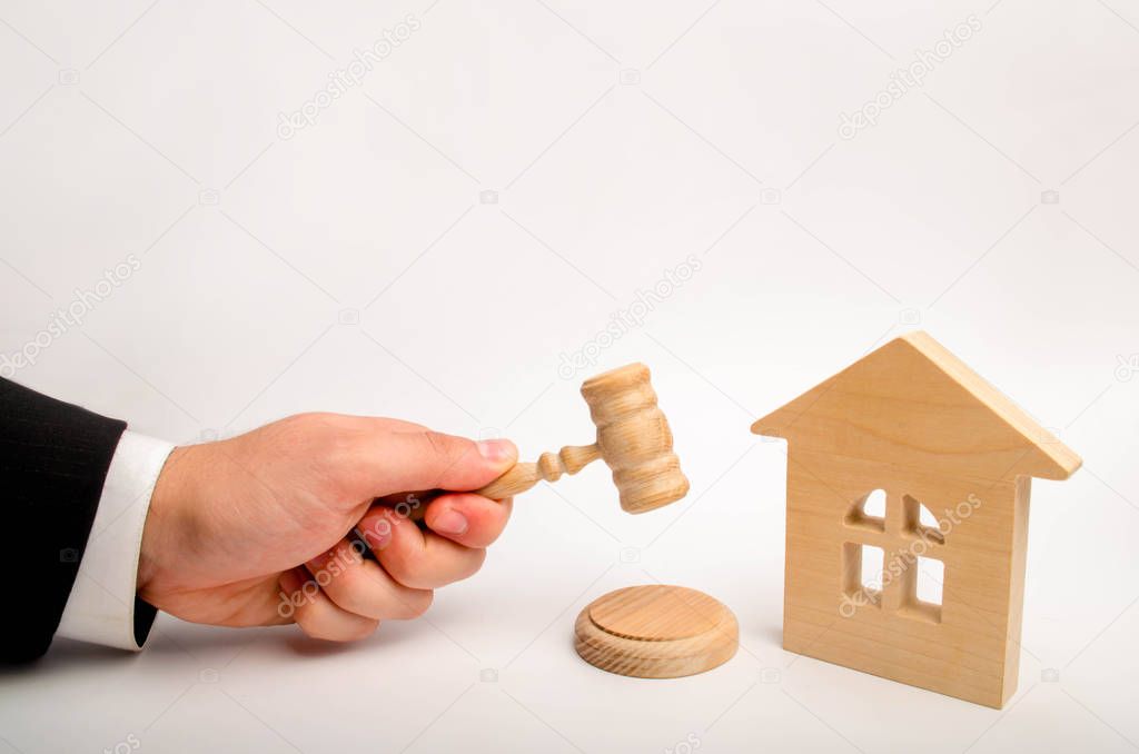 The judge's hand is holding a hammer next to the wooden house. trial of real estate. Elimination and alienation of bankruptcy, confiscation and nationalization. Decision of property disputes.