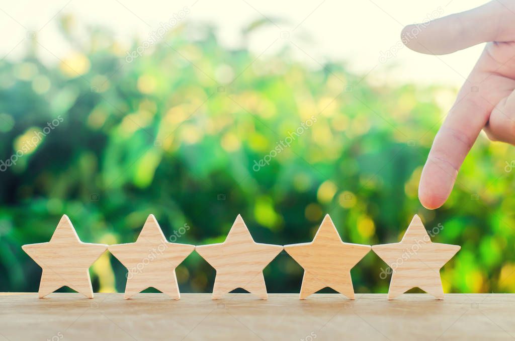 hand points to the fifth wooden star. Get the fifth star. The concept of the rating of hotels and restaurants, the evaluation of critics and visitors. Quality level, good service. selective focus