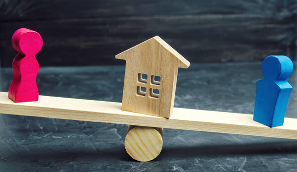 division of property by legal means. clarification of ownership of the house. wooden figures of people. man and woman are standing on the scales. trial, conflict. court. divorce