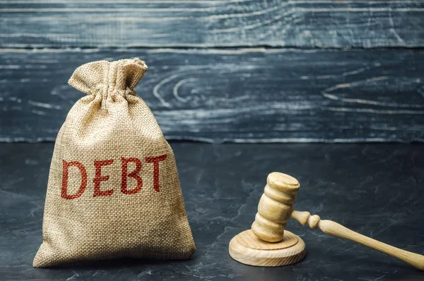 A bag of money and the word Debt and the hammer of the judge. Payment of taxes and of debt to the state. Concept of financial crisis and problems. Risk management. Debt exemption. Credit and loan