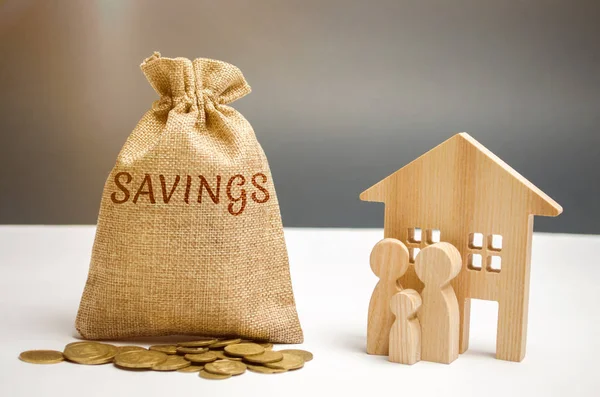 A bag with money and the word savings and a wooden house. The concept of real estate purchase. Buy a house, apartment. Property. Affordable housing. Accumulation and saving money. Home rent