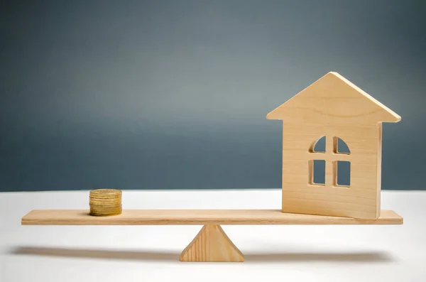 Wooden house with coins on the scales. The concept of real estate purchase. Sale of property. Payment of the mortgage. Redemption of taxes. Tax refund. Credit for the apartment.