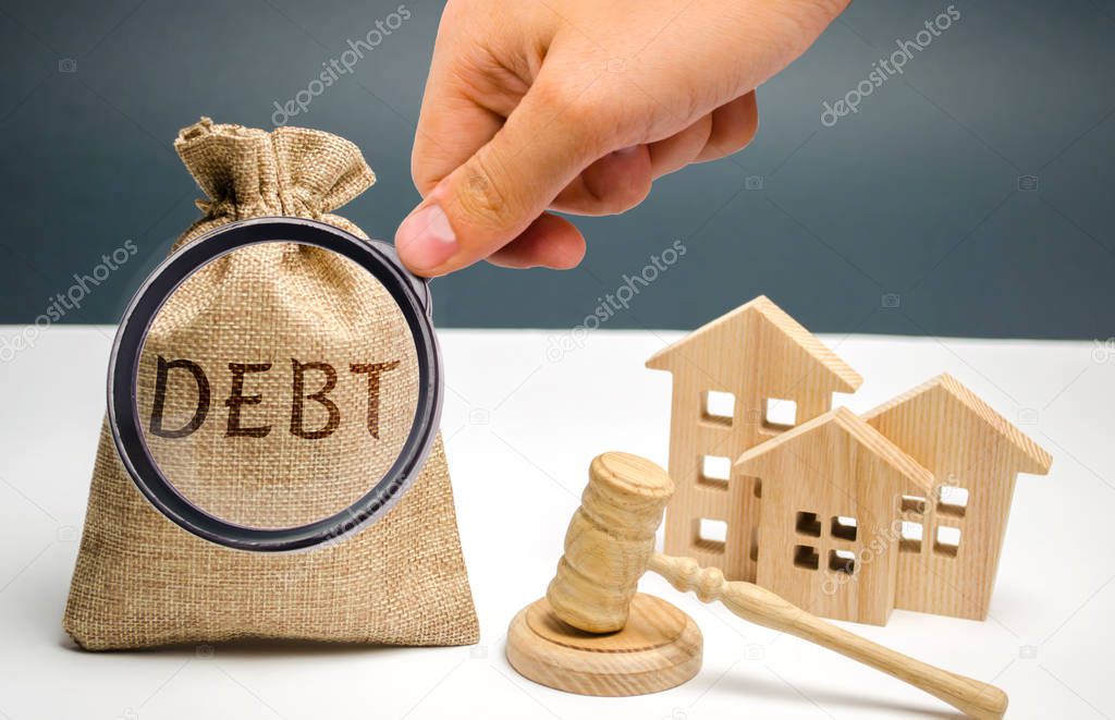 Money bag with the word debt, wooden houses and hammer judge. The concept of debt for housing. Mortgage. Real estate, home savings, loans market concept. Risks of buying a house. Justice and law