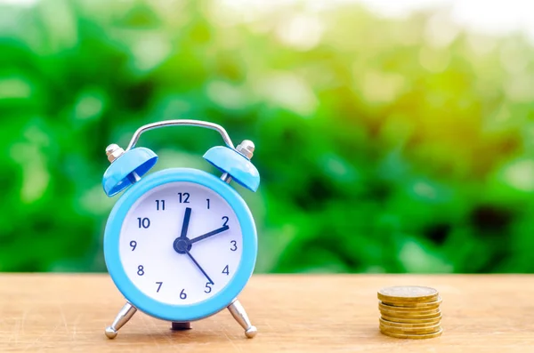 Alarm clock and money on green bokeh background. The concept of Time is money. Business financial ideas. Saving. Financial investments, revenue increase, budget management, savings account