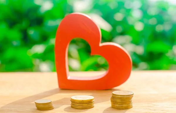 Red wooden heart and money. The concept of saving and accumulation money. Health charity. Donation. The purchases of Valentine\'s Day. Soft selective focus on the coins