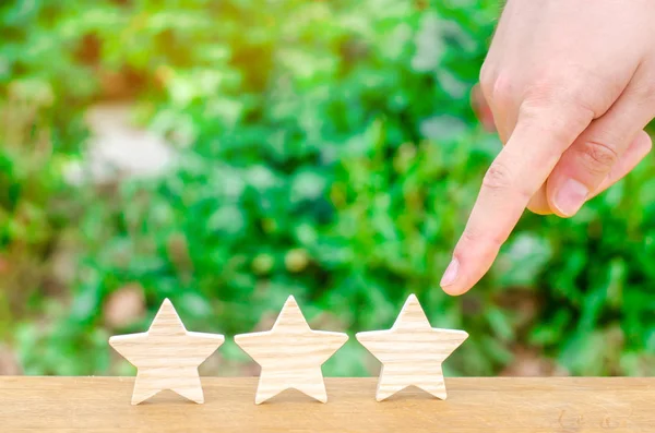 The hand points to the third star on a green background. Rating, level of quality. Universal recognition, success and high efficiency. Evaluation of the hotel or restaurant. Application in the market.