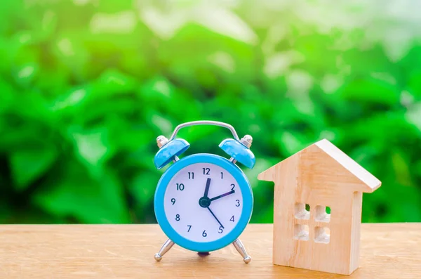 木造住宅と緑の背景に青の目覚まし時計 家賃は毎月住宅と時間の概念 一時的な手頃な価格の宿泊施設 ホテル ホステル 家を買うための融資 — ストック写真