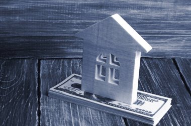 A wooden house stands on a stack of dolor banknotes. The concept of buying and selling immovability, rent of apartments. Credit and mortgage, affordable housing. Utilities payments clipart