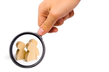 Magnifying glass is looking at the Three people stand together and talk. Three wooden figures of people conduct a conversation on a white background. Communication, meeting place.Selective focus
