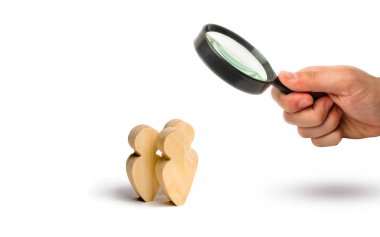 Magnifying glass is looking at the Three people stand together and talk. Three wooden figures of people conduct a conversation on a white background. Communication, meeting place.Selective focus