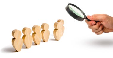 Magnifying glass is looking at the Wooden figures of people stand in the formation. Candidate, elected employee, the best of all. Selection, the choice of talent. Business training. Selective focus