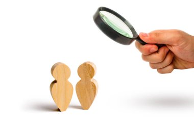 Magnifying glass is looking at the Two people stand together and talk. Three wooden figures of people conduct a conversation on a blue background. Communication, meeting place. Selective focus
