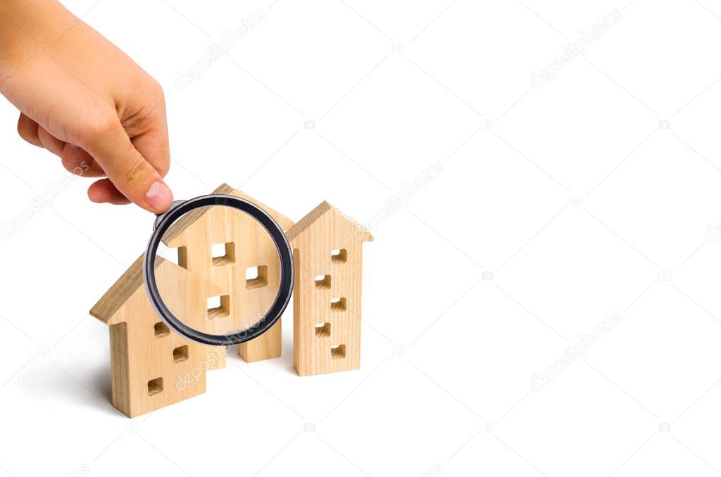 Magnifying glass is looking at the Wooden houses on a white background. The concept of rising prices for housing or rent. Growing demand for housing and real estate. The growth of the city.