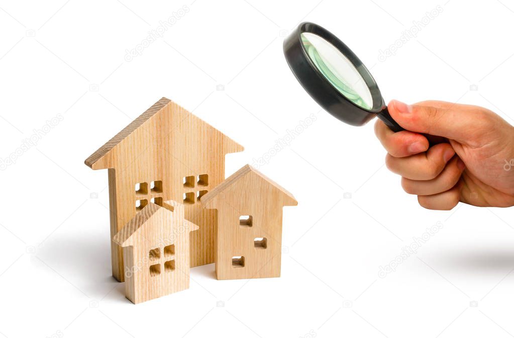 Magnifying glass is looking at the City of wooden houses on a white background. The concept of urban planning, infrastructure projects. Buying and selling real estate, building new buildings, offices