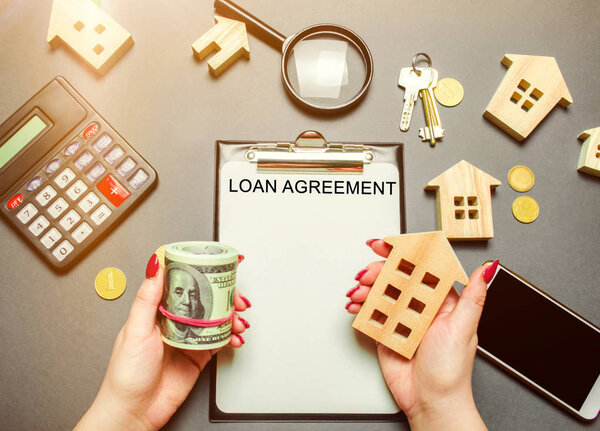 Таблица с деревянными домами, калькулятор, монеты, увеличительное стекло со словом Кредитное соглашение. Договор на приобретение дома или квартиры в кредит. Кредит на недвижимость и недвижимость. Плоский лежал