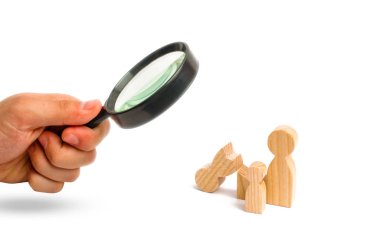 Magnifying glass is looking at a broken wooden figure of a man with a partner and a child. Strife in the family. One parent is broken, addicted to drugs or alcohol, gaming addiction. Single, divorce.