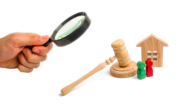 Magnifying glass is looking at the Wooden apartment house with keys and a judge hammer on a white background. The concept of the trial of an apartment house. Confiscation of property.