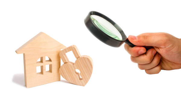 Magnifying glass is looking at the Wooden house with Heart shaped lock on a white background. Love nest, relationships. Buying a house with a young family. Affordable housing. Family psychology