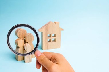 Büyüteç bir ahşap evin yakınındaki aile standları, mavi bir arka plan üzerinde görünüyor. Uygun fiyatlı konut ve ipotek genç aileler ve çiftler için bir ev satın almak için kavramı.