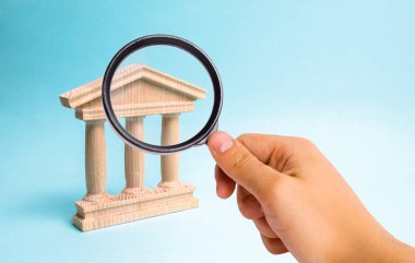Magnifying glass is looking at the Wooden monument or government building. Minimalistic representation of a statebuilding , a courthouse or a monument of history, an ineptration of justice clipart