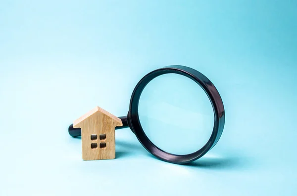 Wooden house and magnifying glass on a blue background. The concept of urban planning, infrastructure projects. Buying and selling real estate, building new buildings, offices and homes. House search.