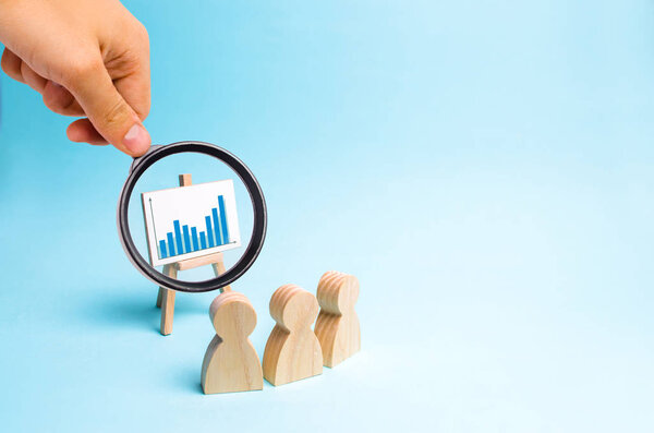 Увеличительное стекло рассматривает трех человек, рассматривающих график и обсуждающих бизнес-стратегию и планы развития компании. Анализ результатов, ознакомительная информация
